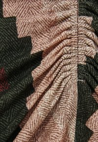 Tessuto in fibra con motivo a spina di pesce nei toni del rosa e del verde, caratterizzato da una texture arricciata e dettagli di cucitura che creano interesse visivo.