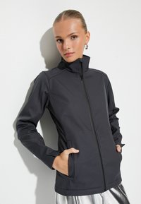 Chaqueta negra con cremallera y cuello alto, con bolsillos laterales y un diseño ajustado, hecha de una tela suave y ligera con detalles de costura.