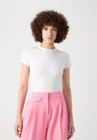 White short-sleeve t-shirt made of smooth fabric, paired with high-waisted pink trousers featuring pleats and a bow detail at the waist.