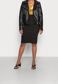 Schwarze Leder-Bikerjacke über einem goldglitzernden Oberteil, kombiniert mit einem schwarzen Bleistiftrock und schwarzen Sandalen mit Blockabsatz. Einfaches, elegantes Design.