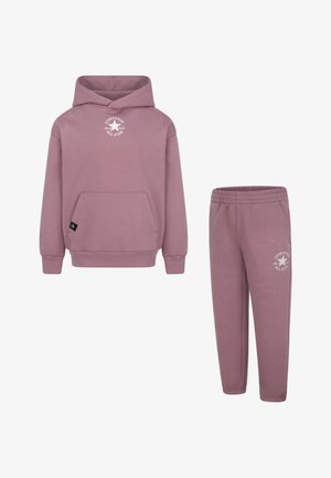 Roza kapuca in usklajene trenirke iz mehkega materiala. Značilnosti vključujejo sprednji žep in logotip na obeh kosih. Elastičen pas na hlačah.