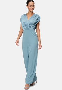 Hellblauer Jumpsuit mit tiefem V-Ausschnitt, gefalteten kurzen Ärmeln und weiter Beinform. Gefertigt aus glattem Stoff mit matter Oberfläche.