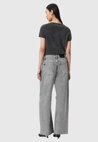 Grijze gebreide top met korte mouwen, gecombineerd met hooggewaist grijze jeans met wijde pijpen, voorzien van achterzakken en een gestructureerde afwerking.