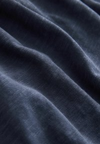 Tissu bleu foncé avec des plis doux montrant un tissage fin et texturé, ainsi que des variations subtiles de lumière et d'ombre.