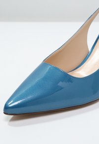 Chaussure slingback en cuir verni bleu à bout pointu avec intérieur beige et semelle basse marron, présentée sur un fond blanc.