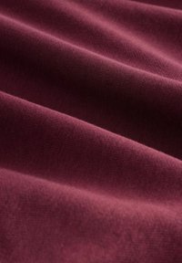 Tessuto bordeaux con una consistenza morbida, che presenta pieghe sottili e una superficie liscia, realizzato in un materiale leggero e elasticizzato.