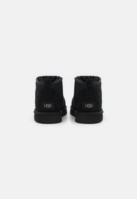 Botas de tobillo de ante negro con forro de lana, que cuentan con una suela de goma plana y una pequeña etiqueta de marca en la parte trasera.