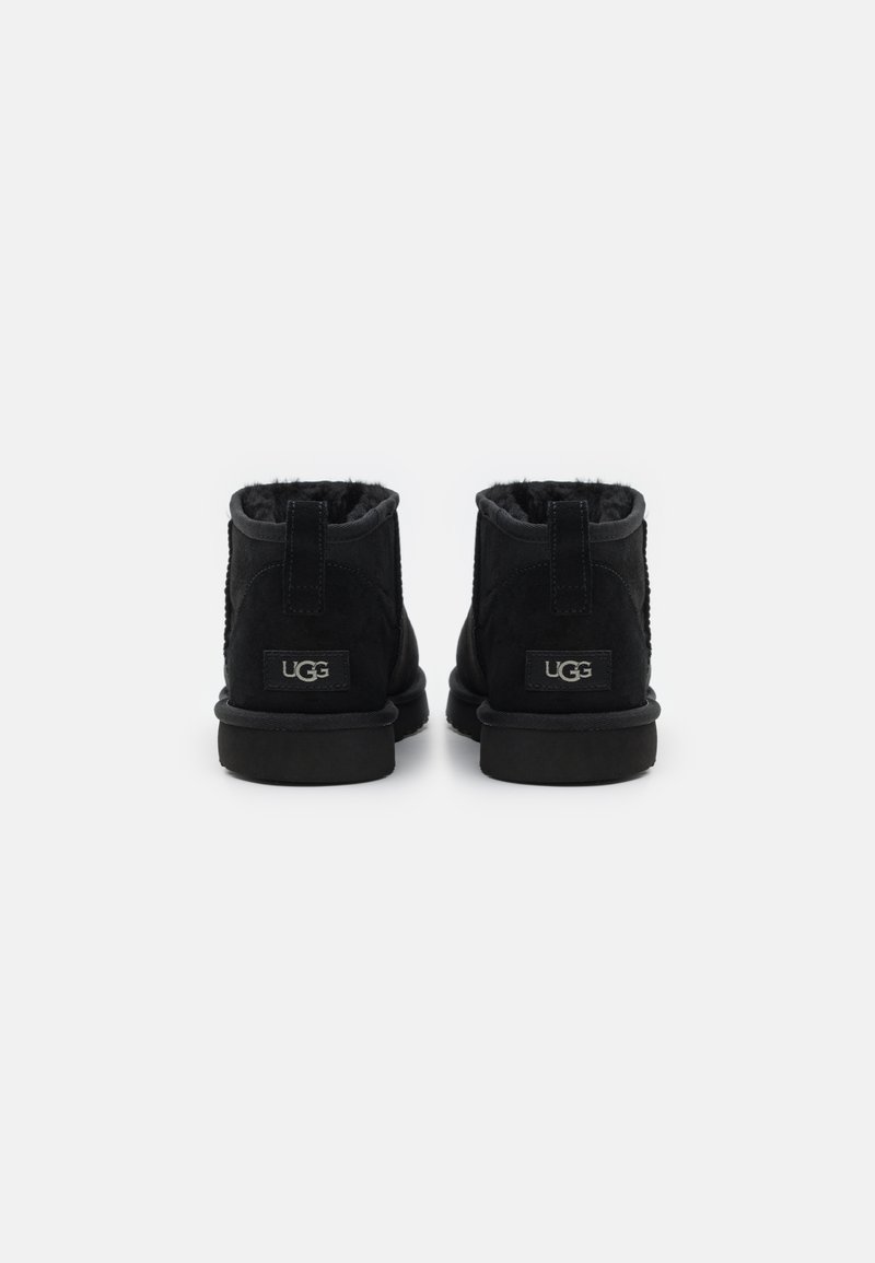 Bottines en suède noir avec doublure en laine, dotées d'une semelle en caoutchouc plate et d'une petite étiquette de marque à l'arrière.