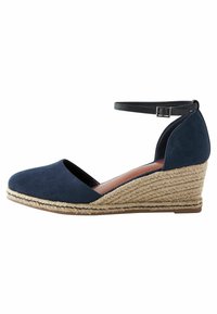 Scarpa in suede blu navy con zeppa e cinturino alla caviglia, caratterizzata da una suola in juta intrecciata e una punta arrotondata. Texture liscia e design strutturato.