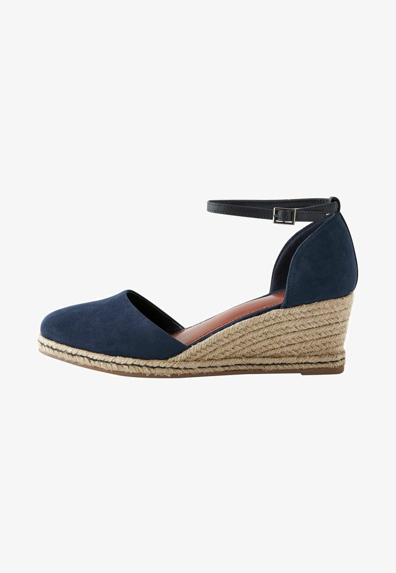 Escarpin en suede bleu marine à talon compensé avec bride de cheville, présentant une plateforme en jute tressé et un bout arrondi. Texture lisse et design structuré.