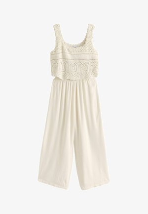 Fehér kezeslábas, textúrált horgolt felső résszel és széles, pliszírozott lábakkal. Négyzet alakú nyakkivágással és spagetti pántokkal rendelkezik. Puha anyag.