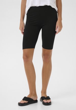 Schwarze Baumwolljersey-Radhosen mit elastischem Bund, körpernahem Schnitt und glatter Textur, kombiniert mit schwarzen flachen Sandalen.