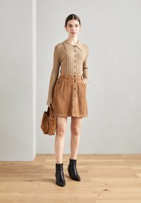Bruine geribde lange mouw top met een kraag, gecombineerd met een beige A-lijn rok van ribfluweel met knopen en zakken. Zwarte enkellaarsjes en een bruine tas.