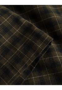 Vihreäja musta ruudullista kangasta, jossa on pehmeä rakenne. Sisältää ohuita valkoisia ruutulines-si ja villamaisen materiaalin, taitettuna reunoilta.