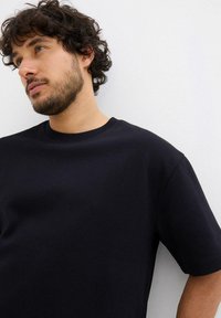 T-shirt nera a maniche corte con finitura testurizzata e scollatura rotonda, caratterizzata da una vestibilità comoda e un design minimalista.