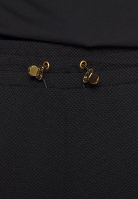 Tessuto nero testurizzato con due accessori in metallo dorato, dotati di clip e cordini in vita per una vestibilità regolabile.