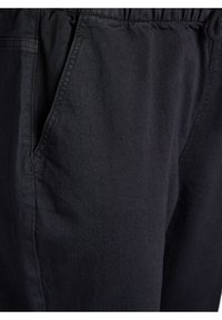 Pantalones negros de mezcla de algodón con cintura elástica, bolsillos laterales y una textura suave; costuras visibles a lo largo de las costuras.