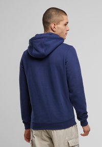 Felpa blu navy realizzata in tessuto morbido con cappuccio regolabile, polsini e orlo a coste, caratterizzata da una superficie liscia e una vestibilità comoda.