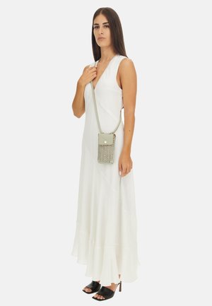 Sac à bandoulière gris clair avec un motif découpé, un rabat supérieur et un fermoir à bouton. Porté sur une robe blanche fluide et associé à des talons ouverts noirs.