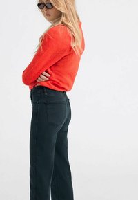 Maglione rosso e peloso abbinato a jeans scuri. Il maglione ha un collo rotondo e maniche lunghe; i jeans hanno una vestibilità classica e tasche posteriori.