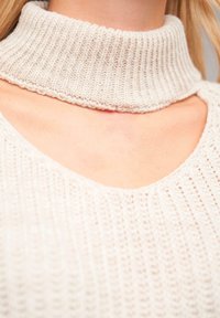 Cream knitted sweater with a high, ribbed turtleneck and a wide, open neckline, featuring a textured fabric and loose fit.