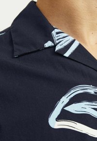Cammicia a maniche corte blu navy con un motivo astratto azzurro chiaro. Il design con colletto presenta una texture liscia e una vestibilità comoda.