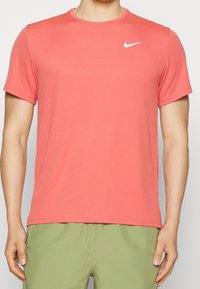 Coral Nike t-shirt in a soft, stretchy fabric. Features short sleeves, a crew neckline, and a white Nike logo on the chest.