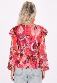 Blusa stampata colorata con maniche a volant, vita elastica e un mix di sfumature rosa, rosso e viola con motivi intricati.