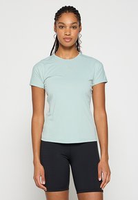 Miętowozielona koszulka sportowa z krótkim rękawem, wykonana z lekkiego i oddychającego materiału. Gładka tekstura w dopasowanym fasonie, zestawiona z czarnymi szortami rowerowymi.