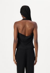 Černá halter top s fitted siluetou, hladkým materiálem a nízkým designem na zádech. Nosit s černými kalhotami na míru.