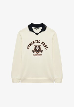 Kermanvärinen huppari, jossa on mustavalkoinen raidallinen kaulus. Siinä on "ATHLETIC DEPT." -teksti ja logo tummanruskeana ja sinisenä.