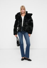 Sort pufferjakke med blank overflate, oversized krage og knappelukking. Kombinert med blå slengjeans og svarte leppestift, med en liten veske.