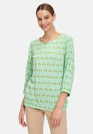 Hellgrüne Bluse mit einem geometrischen Muster in Gelb und Weiß, Rundhalsausschnitt, Dreiviertelärmel und lockerer Passform.