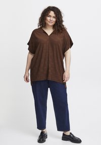 Brun textured kortærmet top med V-udskæring, parret med mørkeblå løstsiddende jeans og sorte slip-on sko.