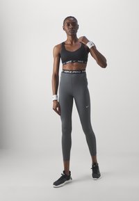 Svart sports-bh med Nike-logo, høyhalsede grå tights med "Nike Pro"-bånd, hvite håndleddsbånd og svarte treningssko.