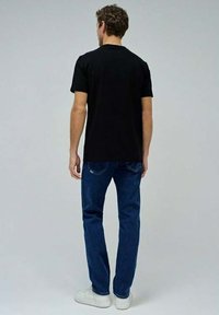 Camiseta negra de algodón de manga corta, cuello redondo, combinada con jeans de denim azul, llevada con zapatillas blancas. Detalles de costura visibles.
