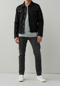 Chaqueta de mezclilla negra con botones plateados, camiseta gris, pantalones vaqueros gris oscuro y zapatillas blancas. La chaqueta tiene dos bolsillos en el pecho y un corte clásico.