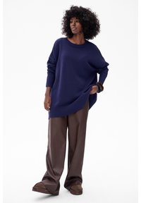 Navyblauw oversized trui met geribde manchetten en zoom, gecombineerd met bruin wijde broekspijpen en bruine instapschoenen.