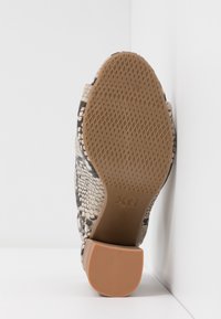 Semelle marron à motifs d'une chaussure à talon haut avec une prise texturée et le nom de la marque Xti embossé près de la voûte plantaire.