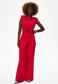 Red two-piece outfit featuring a sleeveless top with a knotted front and wide-leg pants. Smooth fabric with a solid color and no patterns.