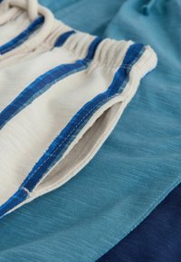 Katoenen stof met een mix van blauwe tinten, voorzien van een gestructureerd oppervlak en een witte elastische tailleband met blauwe gestreepte accenten.