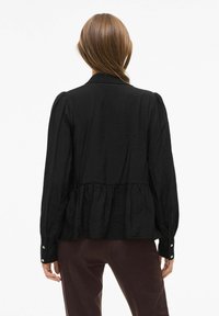 Crna bluzica s teksturiranim materijalom, dugim rukavima, nabranim pojasom i manžetama na dugmad, sadrži suptilni sjaj i ležeran kroj.