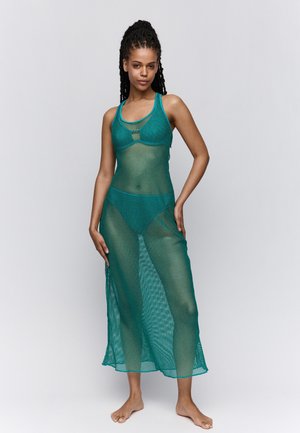 Türkisfarbener Mesh-Look mit einem enganliegenden Bralette und einem langen, durchsichtigen Rock mit Seitenschlitzen, die den passenden Bikini darunter zeigen.