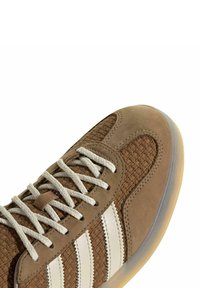 Sneaker marrone con tessuto intrecciato testurizzato e dettagli in suede, che presenta strisce bianco sporco e lacci beige, punta arrotondata e suola in gomma.