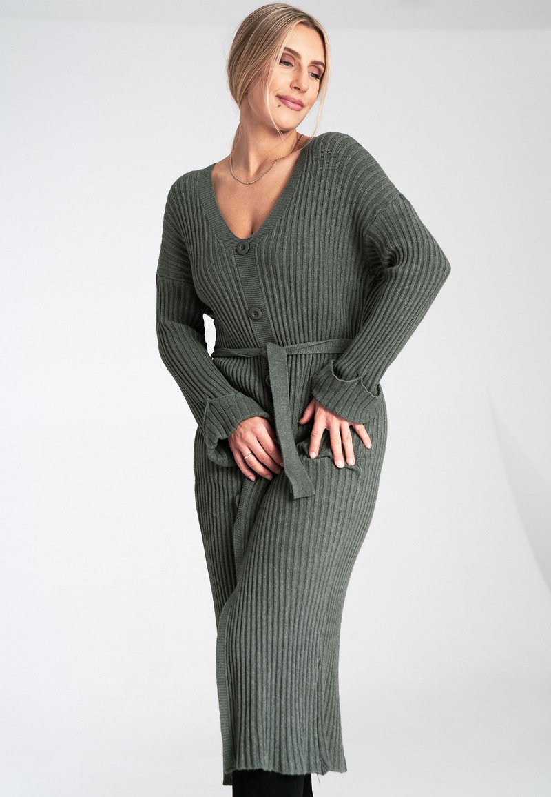 Olivgrüner, gerippter Strickcardigan mit V-Ausschnitt, vorderen Knöpfen und einem Bindegürtel in der Taille. Mit langen Ärmeln und seitlichen Schlitzen.
