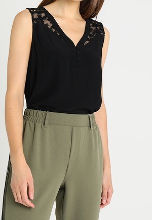 Haut noir sans manches avec détails en dentelle aux épaules et boutons sur le devant, associé à un pantalon taille haute vert olive avec ceinture élastique.