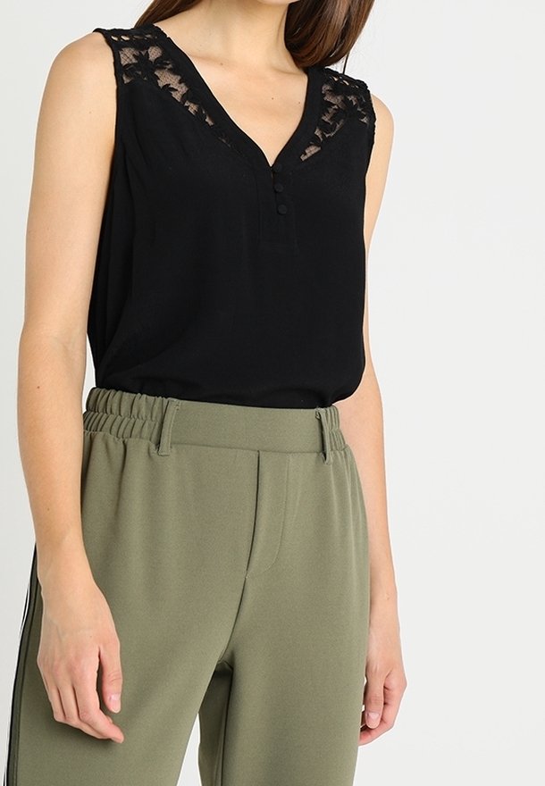 Haut noir sans manches avec détails en dentelle aux épaules et boutons sur le devant, associé à un pantalon taille haute vert olive avec ceinture élastique.