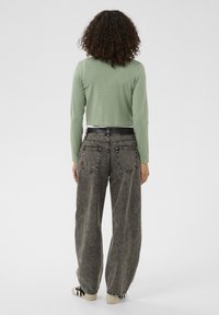 Groen cropped trui met lange mouwen gecombineerd met hooggetailleerde, zwart denim jeans met wijde pijpen en subtiele stiksel op de zakken.
