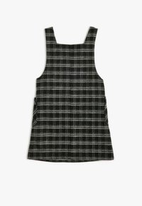 Vestido de cuadros en blanco y negro con tirantes anchos, que cuenta con dos bolsillos laterales, un escote recto y un acabado de tela texturizada.