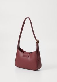Burgundy leather handbag with a curved shape, flat top, short strap, and a magnetic closure. Smooth texture with minimal stitching details.
